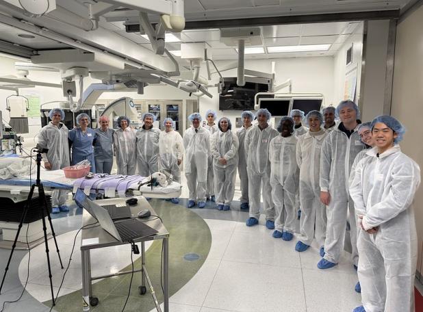 Group of faculty and students in semi-circle in white jumpers in hospital surgical room